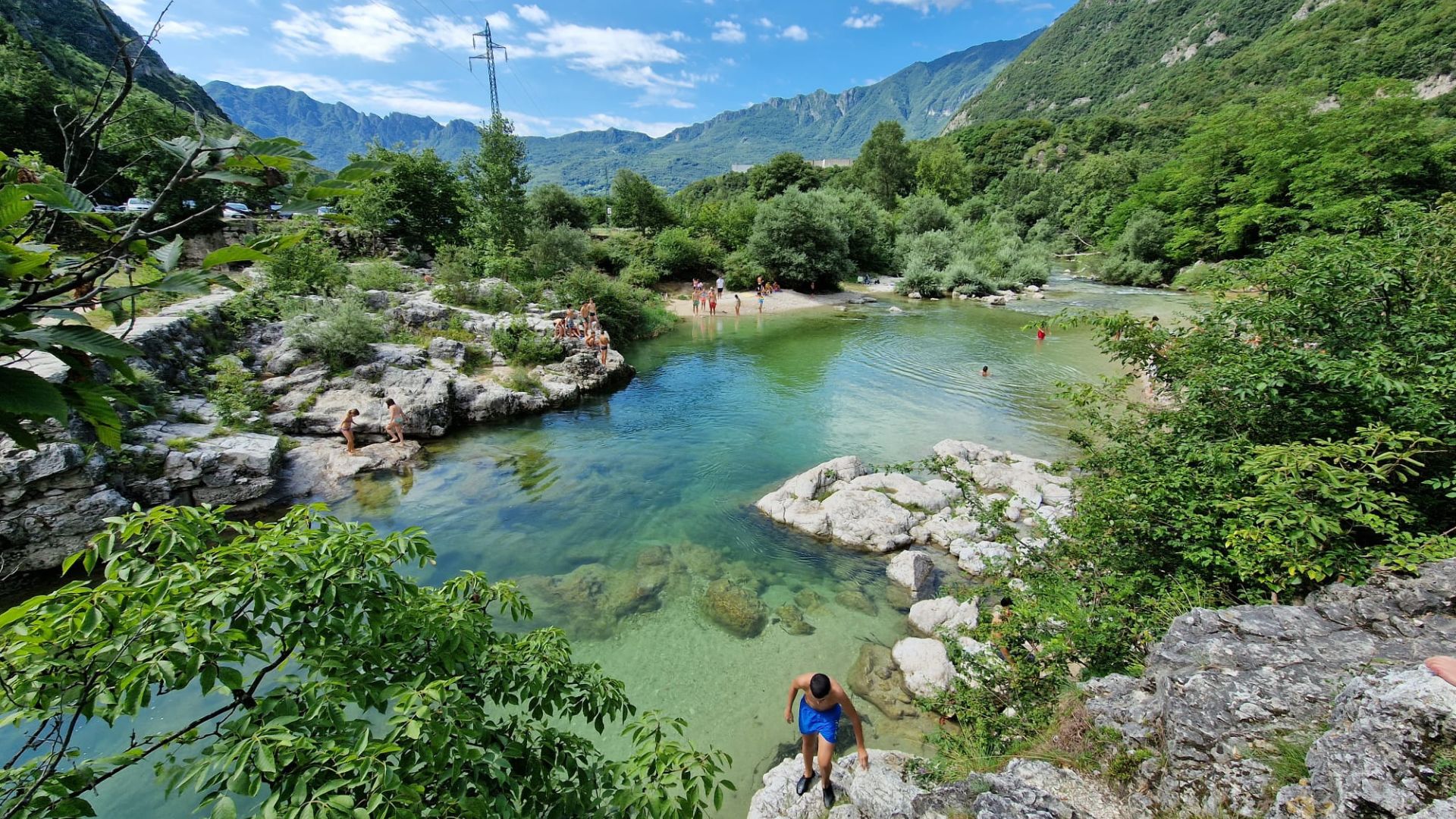Il laghetto naturale dalle acque verdi tra le montagne di Tonezza, con un bambino del camp seduto sulla riva